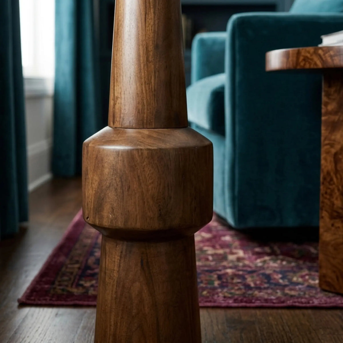 Détail du pied en bois rouge tourné du lampadaire Atlas, fauteuil en velours bleu canard et tapis persan en arrière-plan
