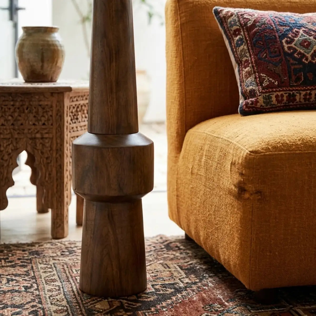 Gros plan sur le pied en bois rouge tourné du lampadaire Atlas à côté d'un fauteuil moutarde et d'un coussin kilim