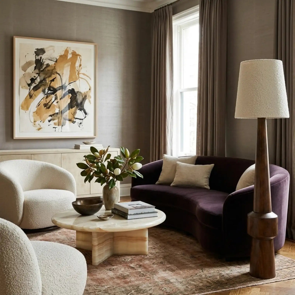 Lampadaire Atlas à côté d'un canapé courbe en velours prune, fauteuils bouclette blancs et table basse ronde