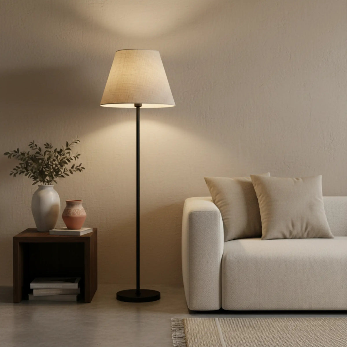 Lampadaire beige allumé entre un canapé blanc et une table de chevet en bois foncé avec vases en terre cuite