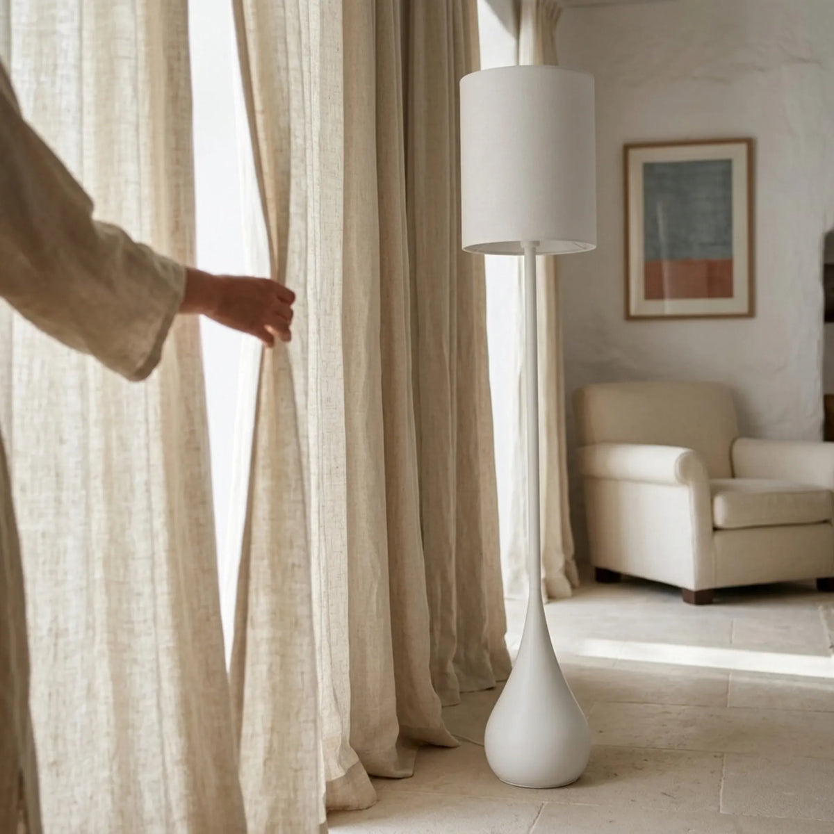 Lampadaire blanc Goutte près de rideaux en lin ouverts sur la lumière naturelle, à côté d'un fauteuil crème