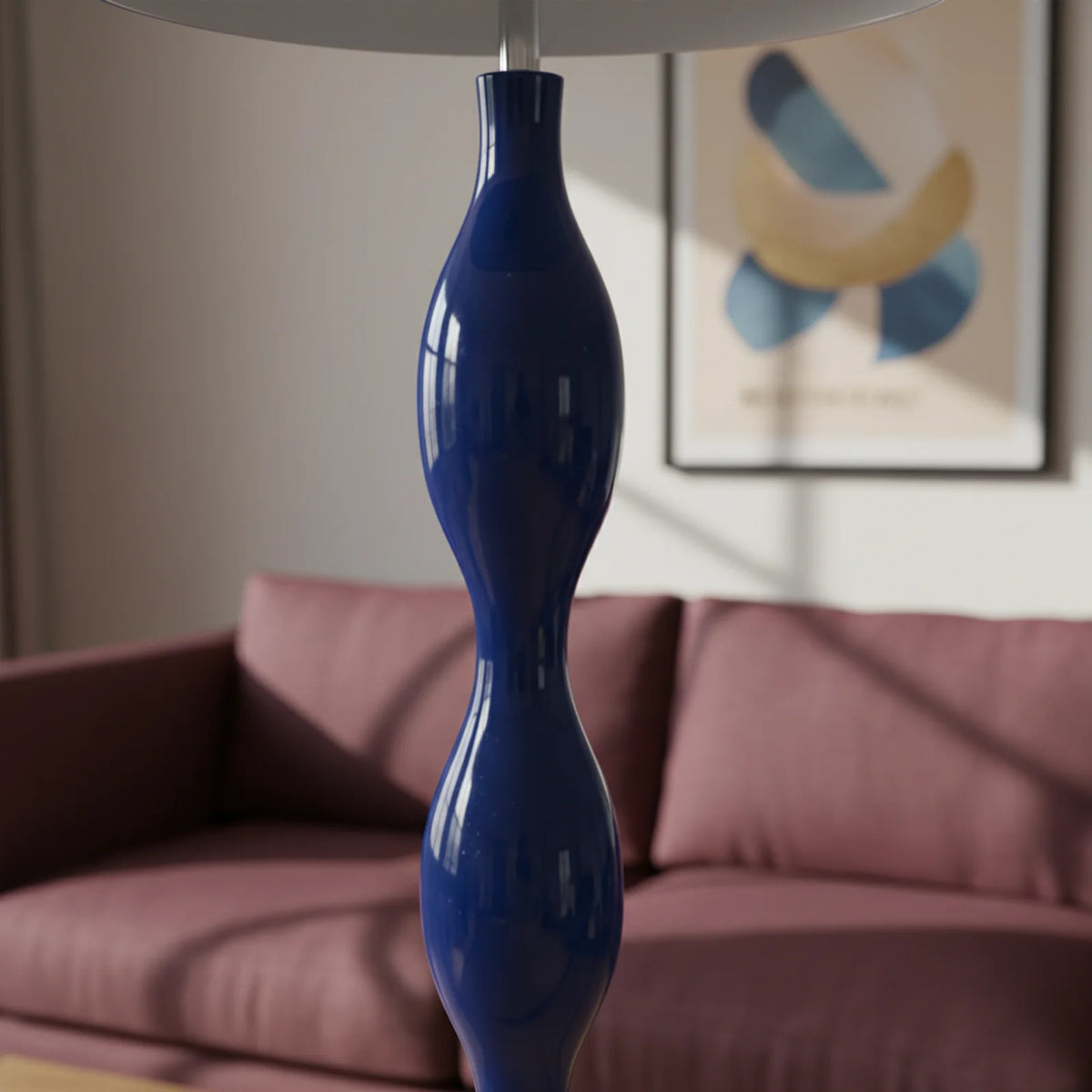 Détail du pied ondulé bleu brillant du lampadaire, devant un canapé rose foncé flou