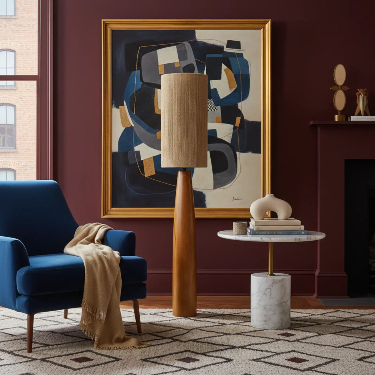 Lampadaire pied bois entre un fauteuil bleu et une table d'appoint en marbre, devant un mur bordeaux