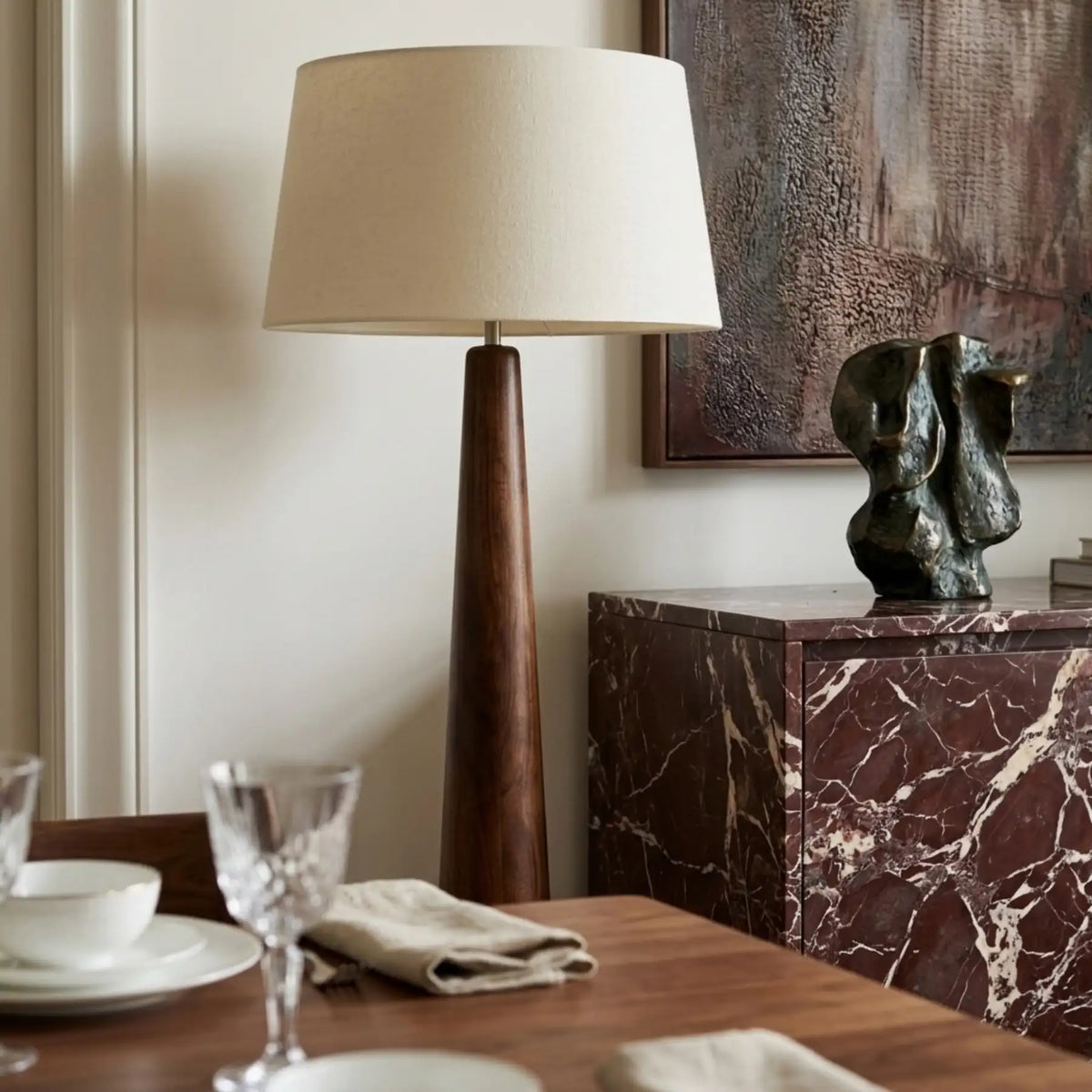 Lampadaire en bois tourné à abat-jour en lin près d'une table dressée et d'un buffet en marbre bordeaux avec sculpture