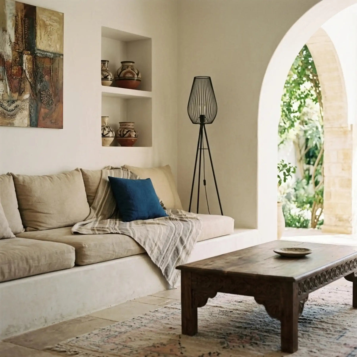 Lampadaire cage goutte dans un salon blanc avec banquette maçonnée, niches murales, porte en arche et table basse en bois sculpté