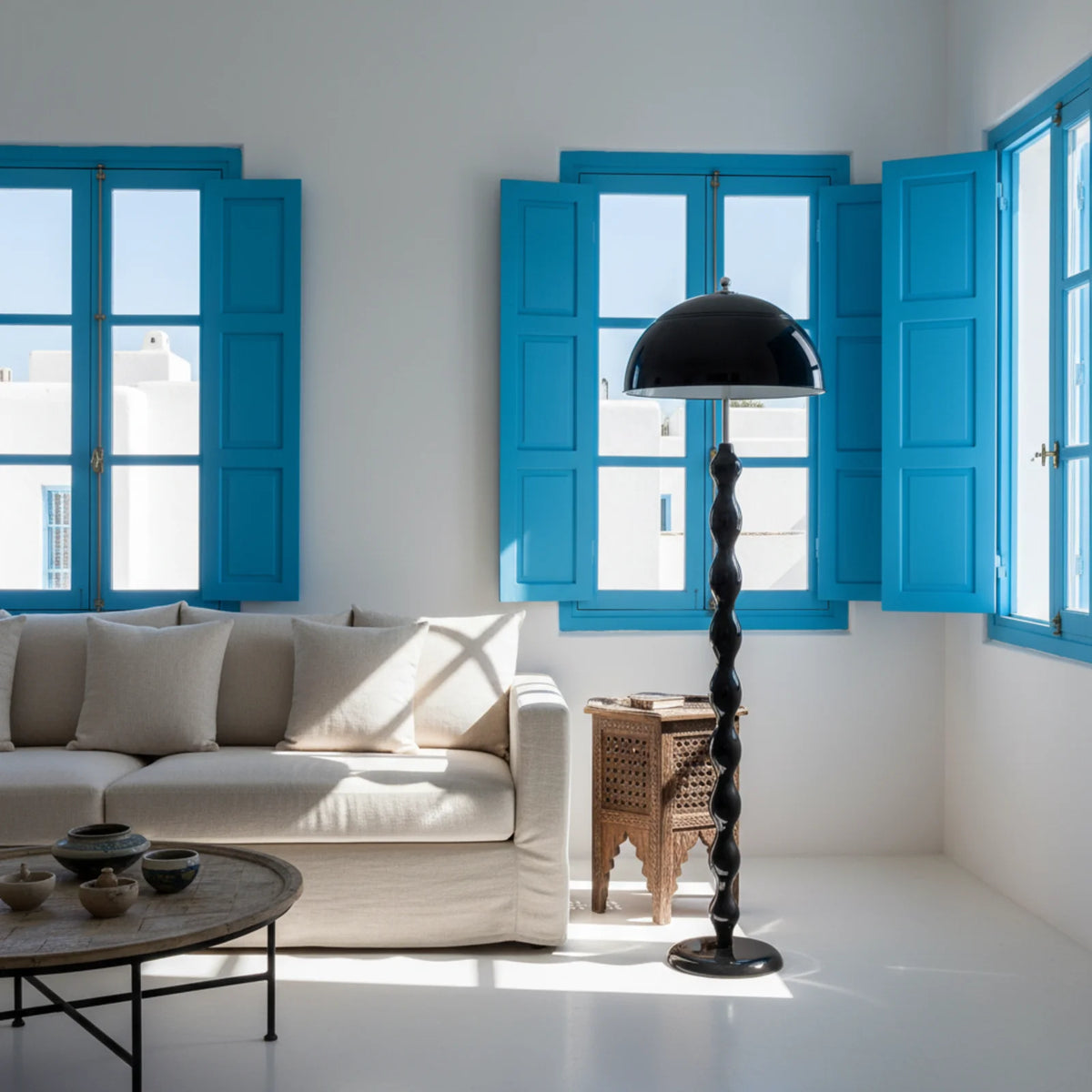 Lampadaire champignon noir dans un salon blanc aux volets bleus de style tunisien, près d'un canapé en lin