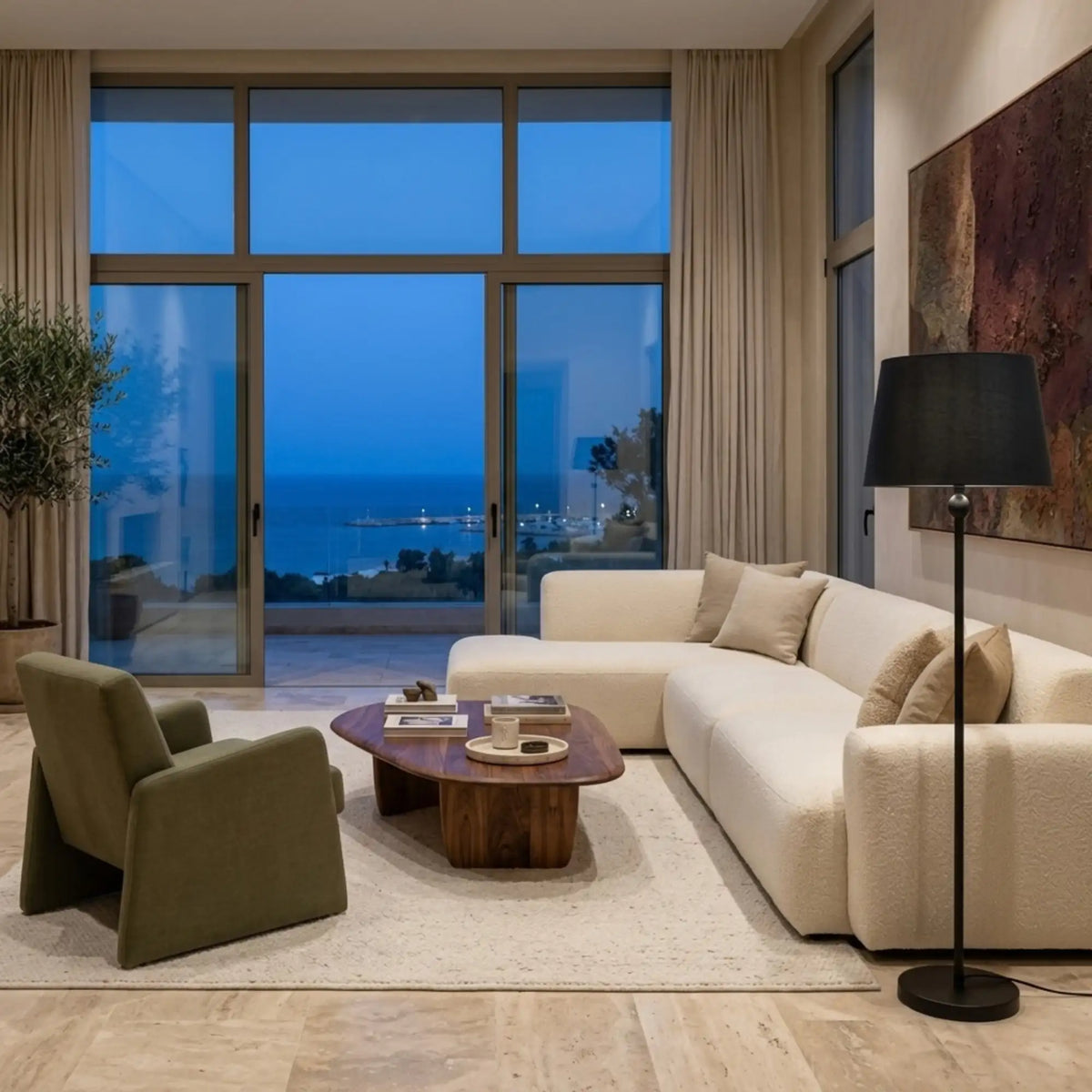 Lampadaire classique noir près d'un canapé d'angle crème, face à une baie vitrée donnant sur la mer au crépuscule
