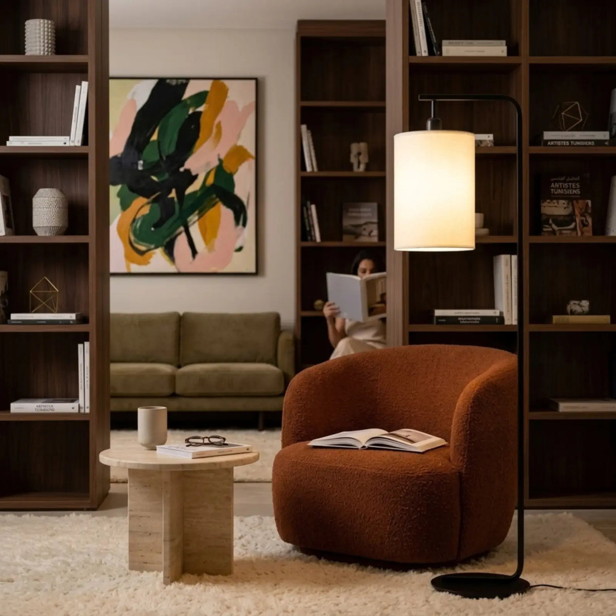 Lampadaire noir allumé à côté d'un fauteuil rouille, dans un coin lecture entouré de bibliothèques en bois