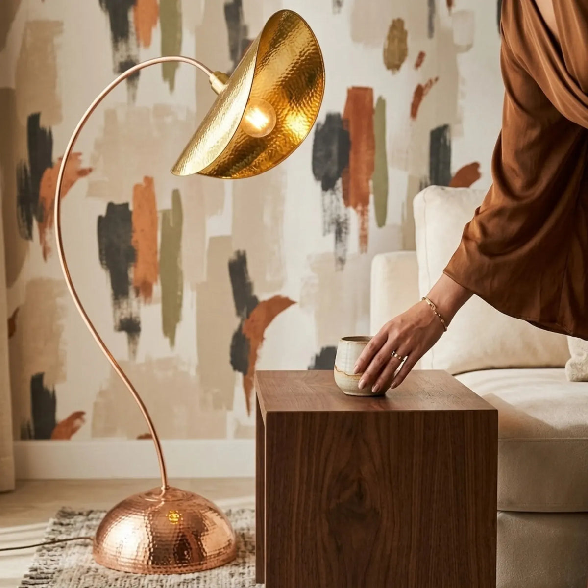 Main posant une tasse sur une table d'appoint en bois, sous l'abat-jour doré du lampadaire en cuivre