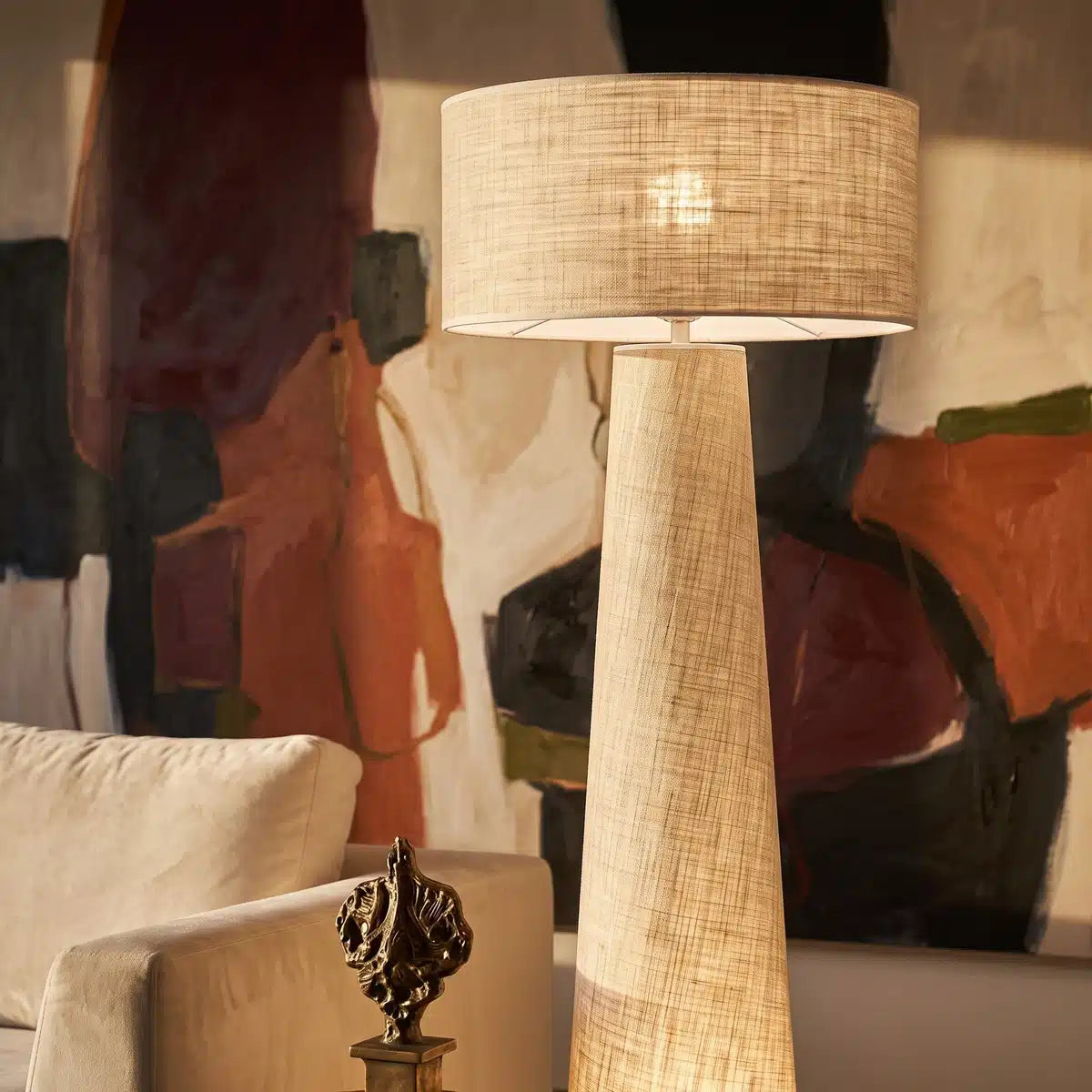 Pied conique et abat-jour tambour en lin du lampadaire, devant un grand tableau abstrait