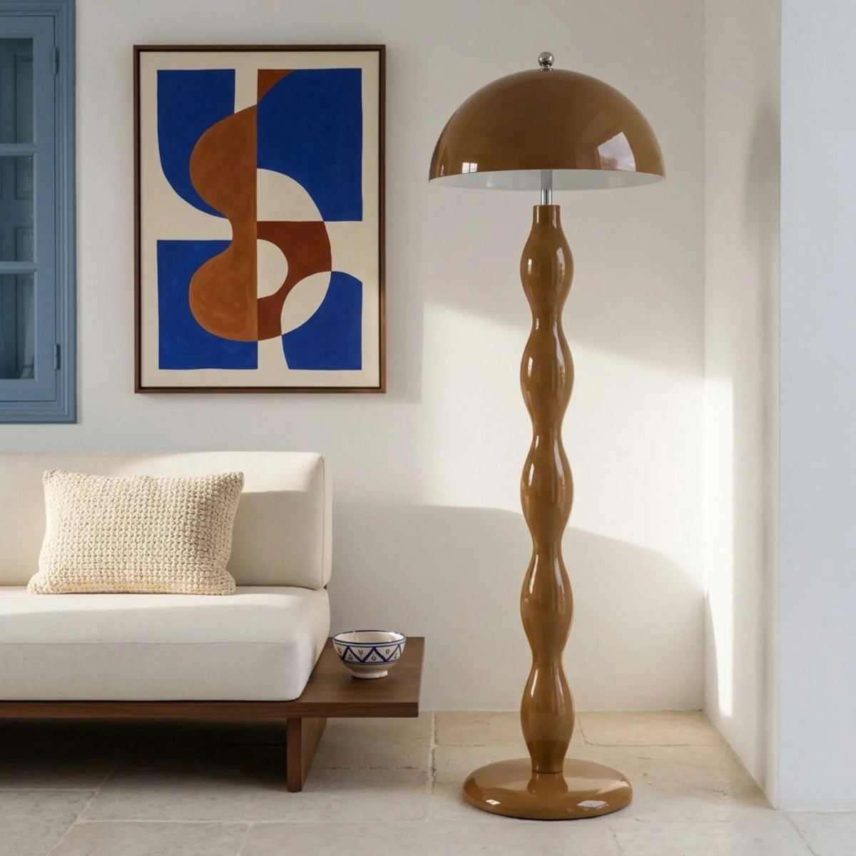 Lampadaire marron dans un salon blanc lumineux, près d'une banquette basse et d'un tableau bleu et terracotta