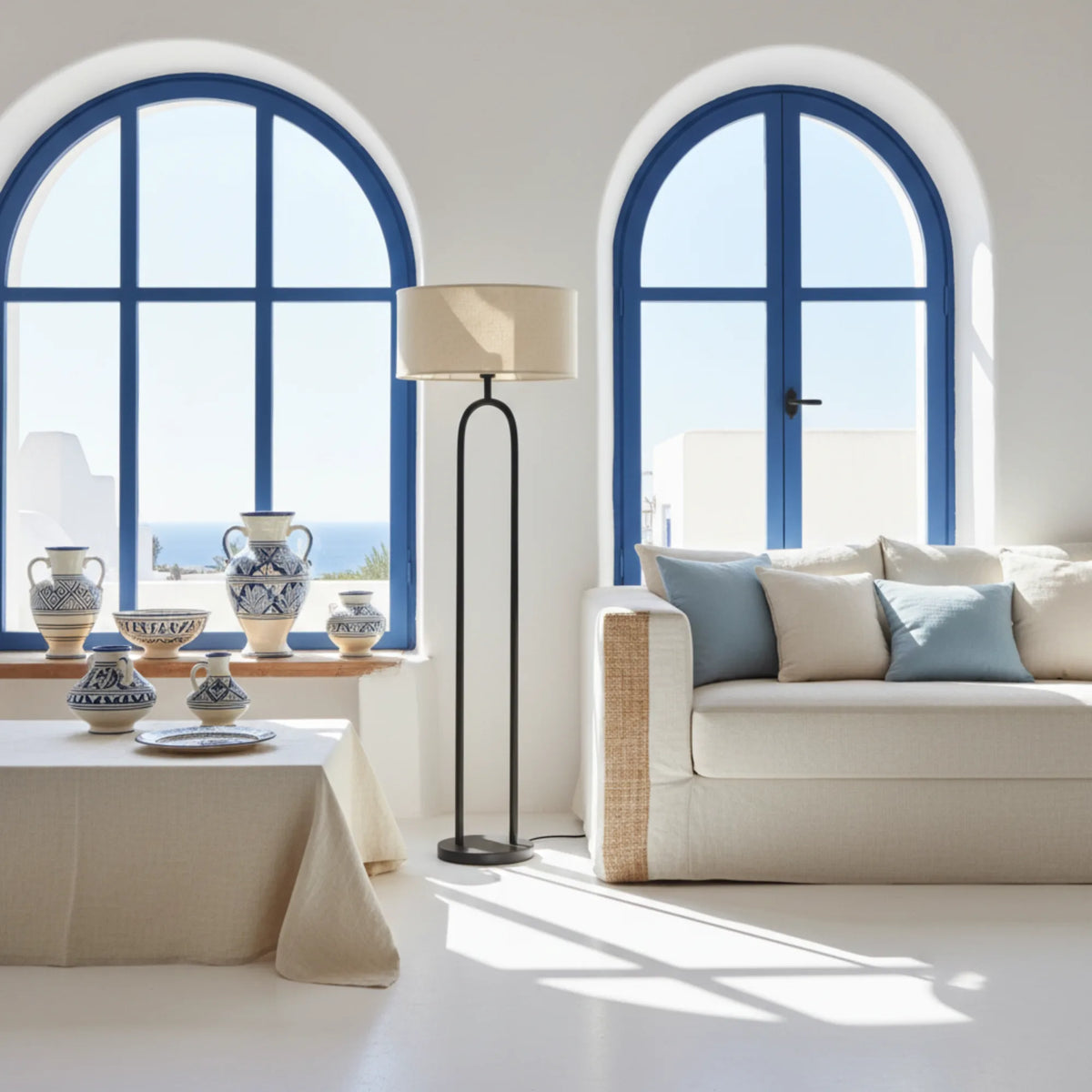Lampadaire design noir dans un salon blanc méditerranéen aux fenêtres en arche bleues et vases en céramique