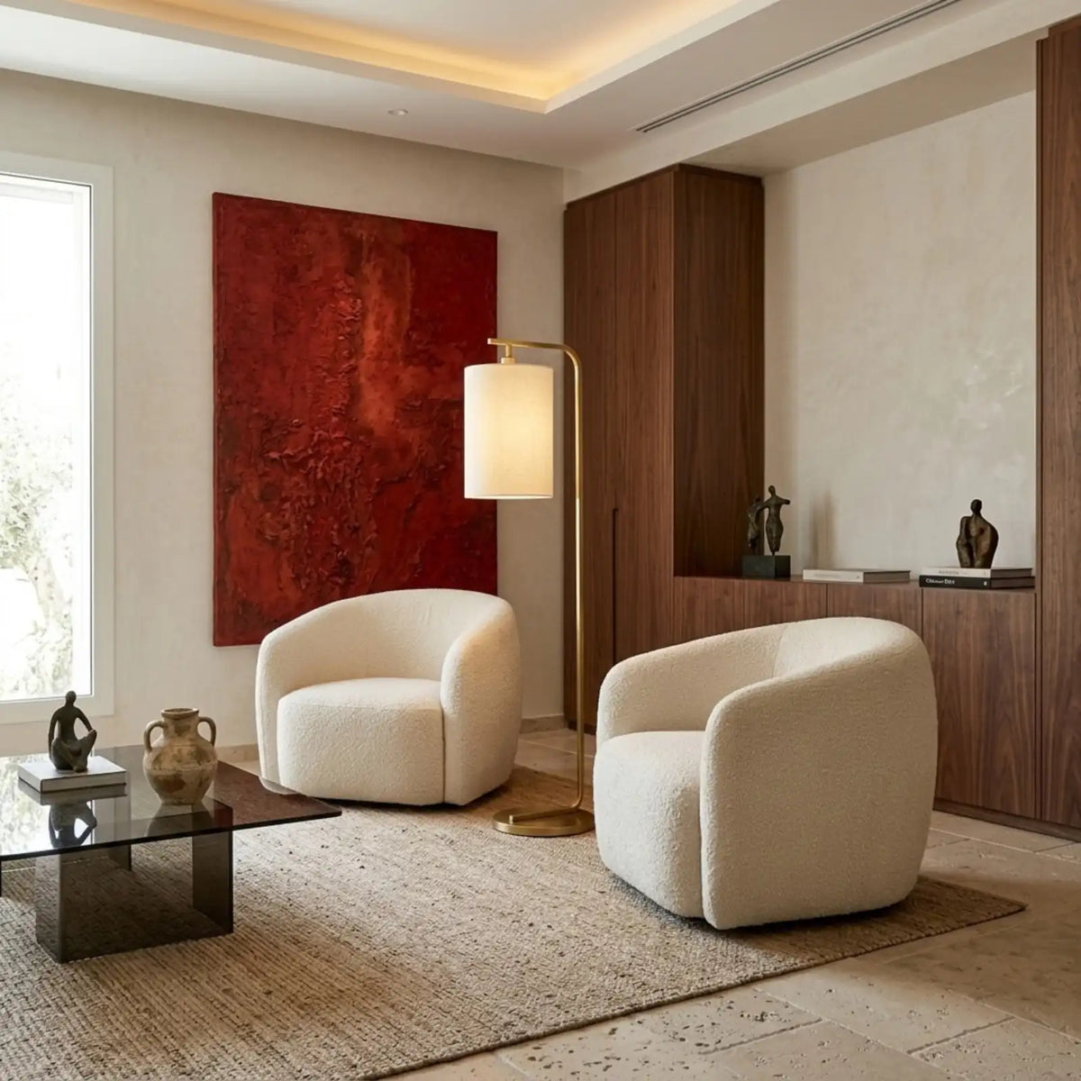 Lampadaire doré entre deux fauteuils bouclés blancs, devant un tableau rouge et un meuble en bois foncé