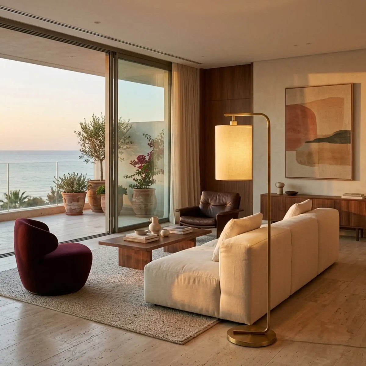 Lampadaire doré allumé derrière un canapé crème dans un salon avec baie vitrée sur la mer