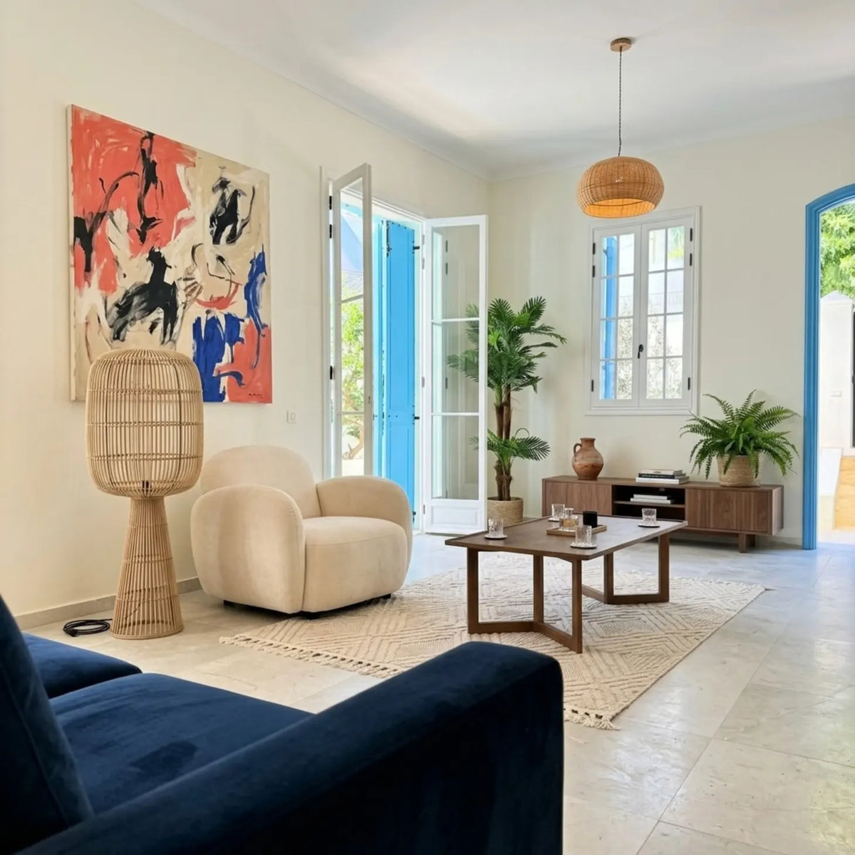 Lampadaire en rotin et suspension en fibres naturelles dans un salon lumineux, près d'un fauteuil bouclette et d'un canapé bleu nuit