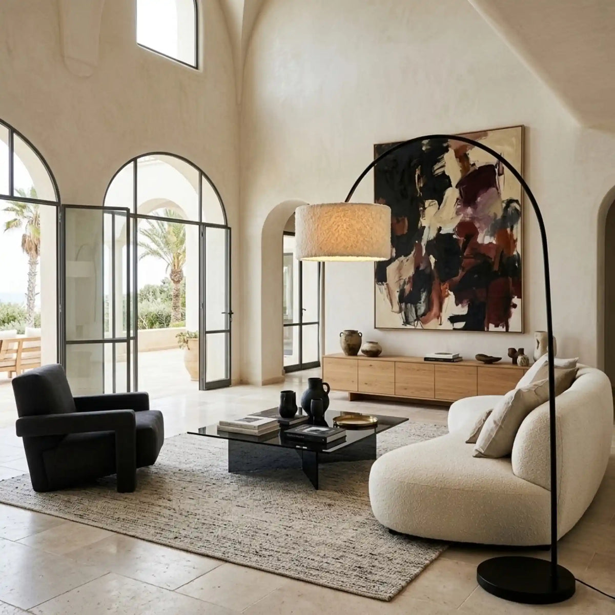 Lampadaire girafe au-dessus d'un canapé arrondi blanc, avec fauteuil noir et fenêtres en arche