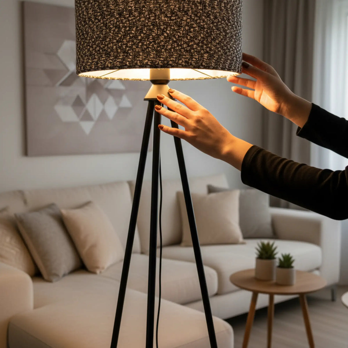 Mains ajustant l'abat-jour chiné allumé du lampadaire trépied noir, canapé beige en arrière-plan
