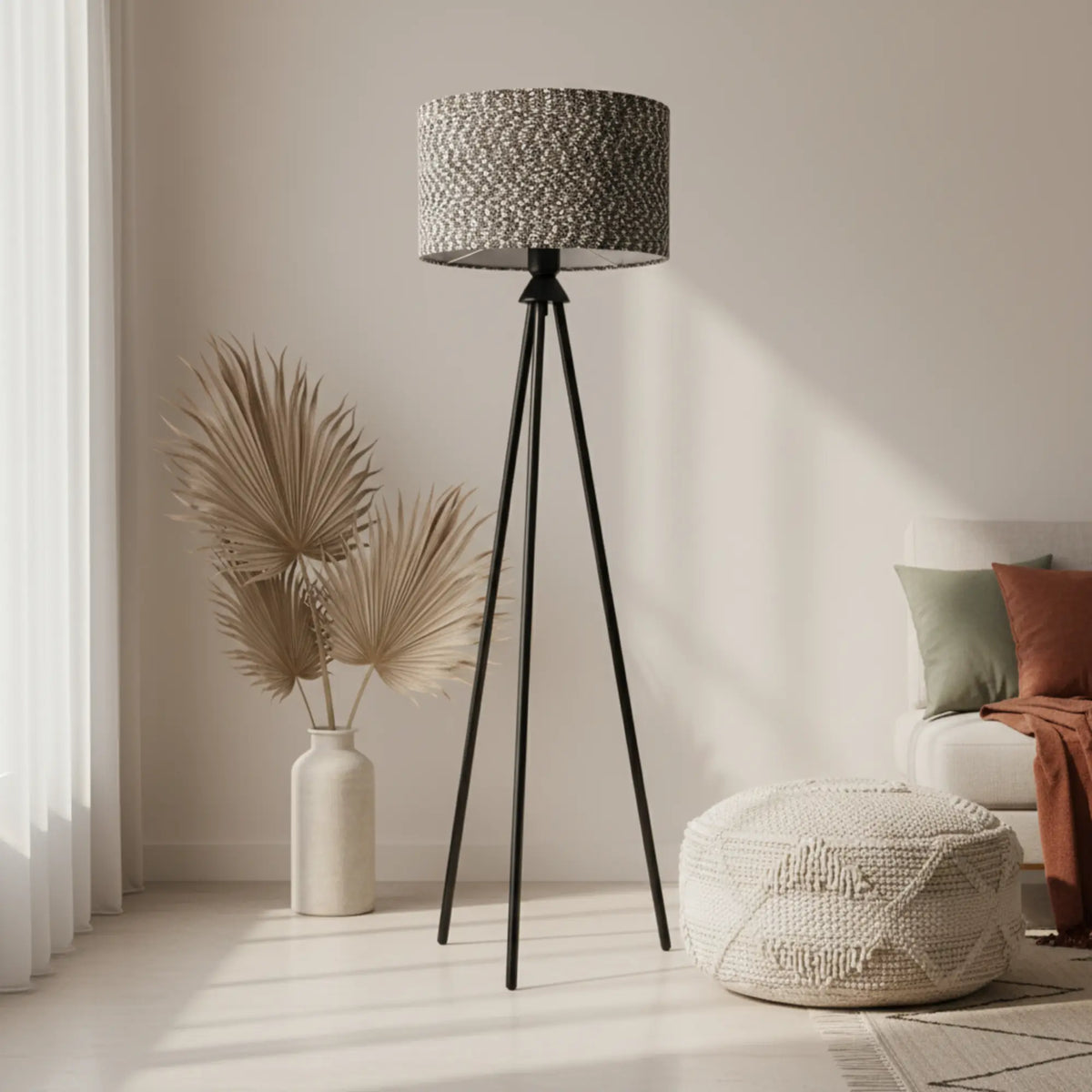Lampadaire trépied à abat-jour chiné dans un intérieur lumineux avec pouf tressé blanc et vase d'herbes séchées