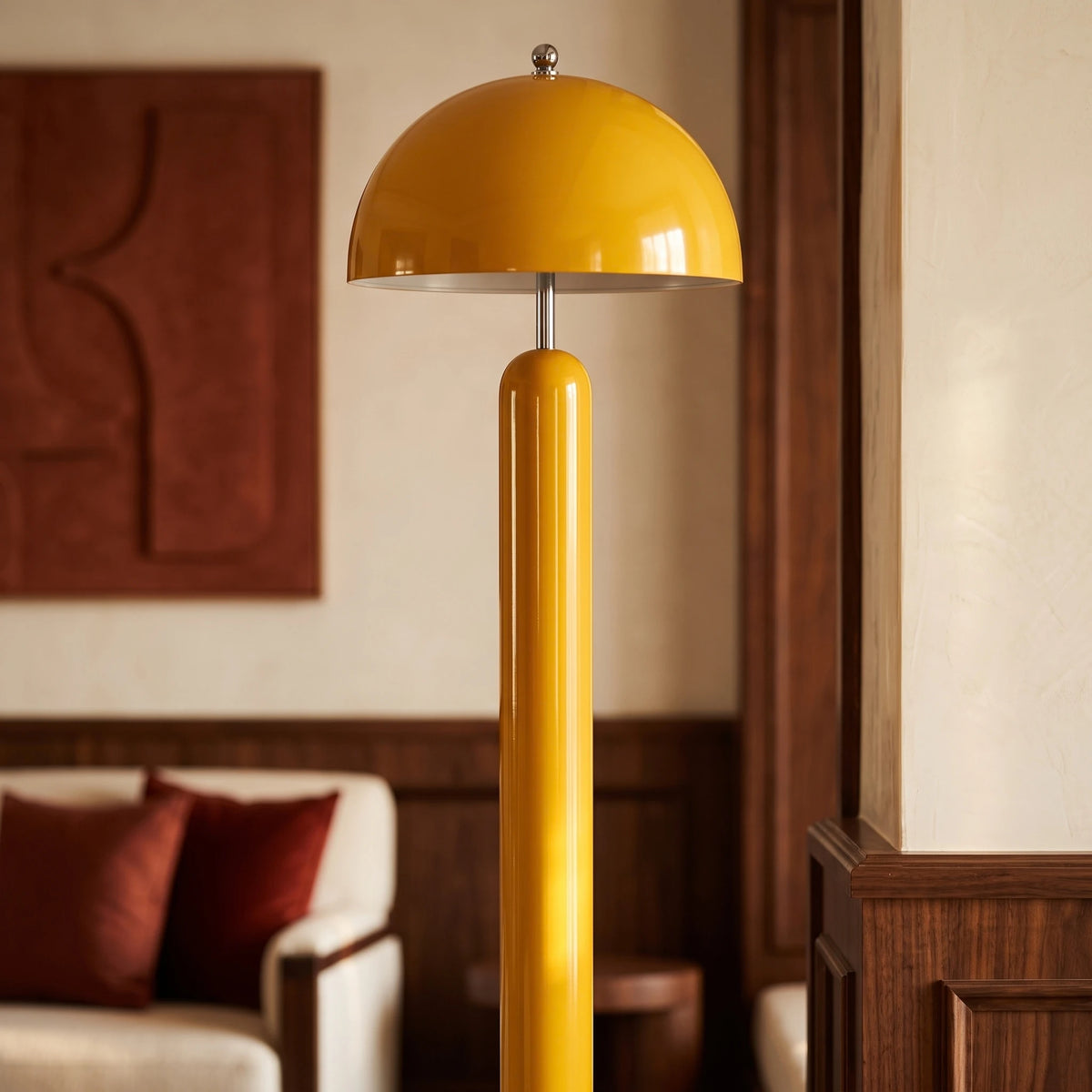 Pied cylindrique et dôme jaune du lampadaire devant un panneau mural terracotta et des coussins bordeaux