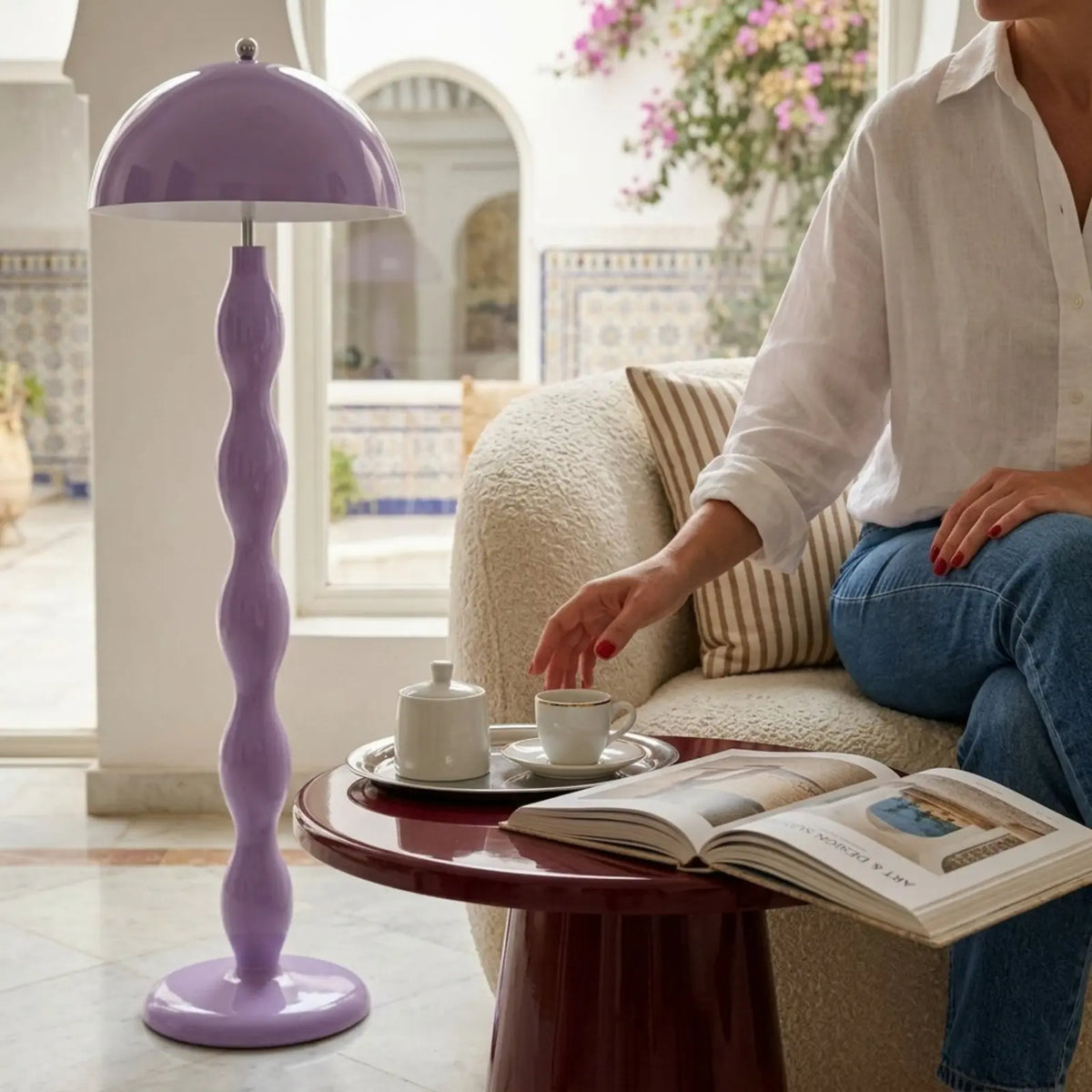 Lampadaire lilas près d'un canapé bouclé et d'une table d'appoint bordeaux, devant un patio aux carreaux de faïence