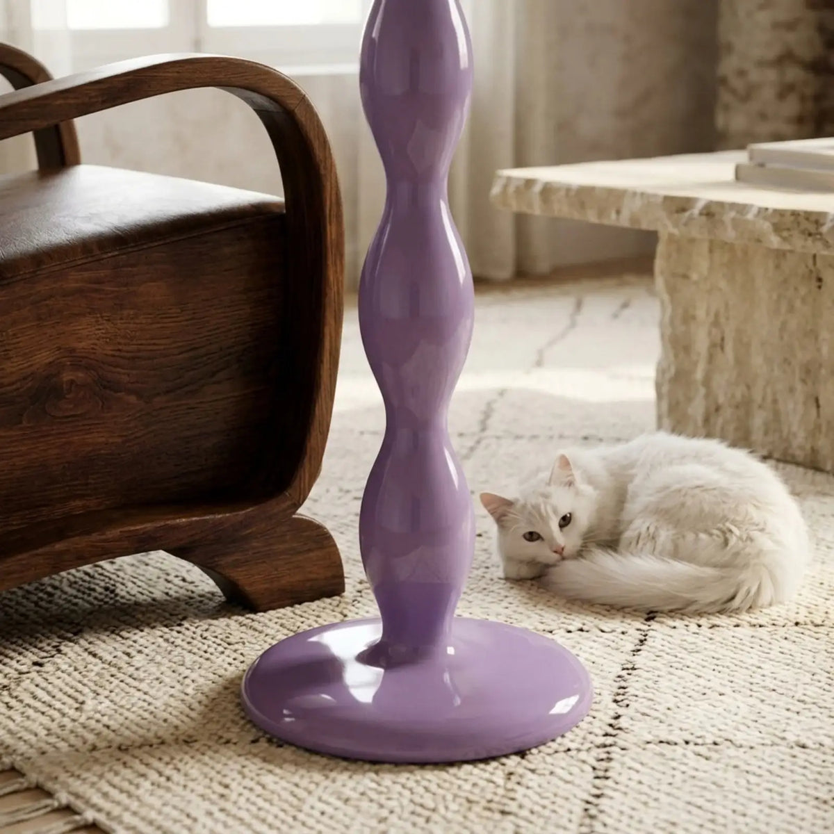 Socle rond du lampadaire lilas sur un tapis berbère, entre un fauteuil en bois et un chat blanc