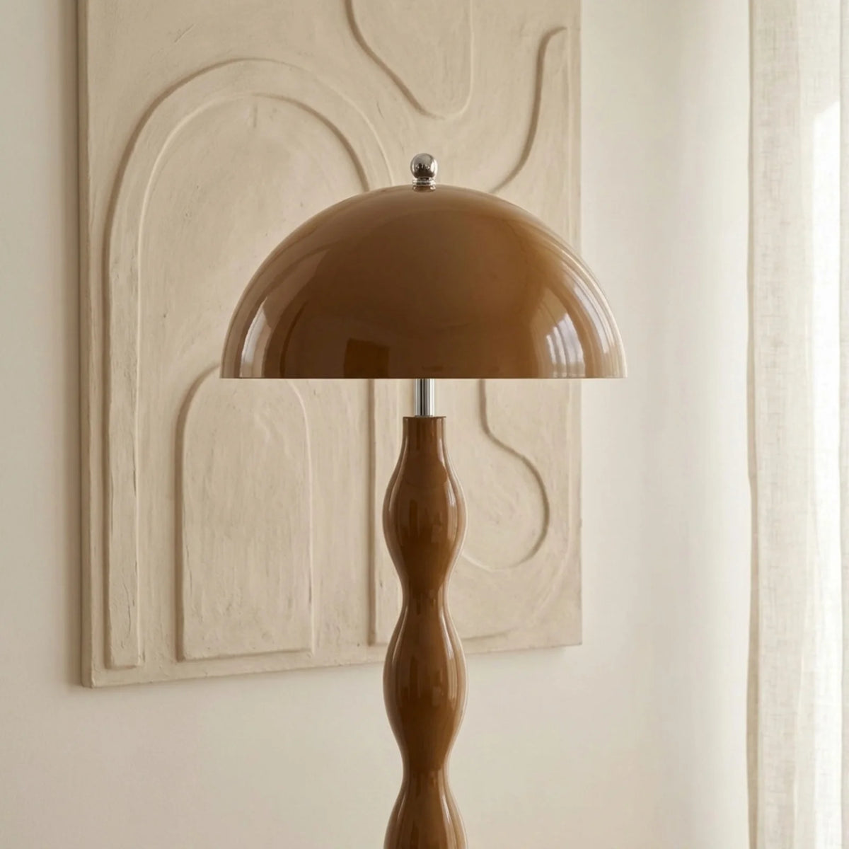 Gros plan sur l'abat-jour champignon marron du lampadaire, devant un bas-relief en plâtre crème