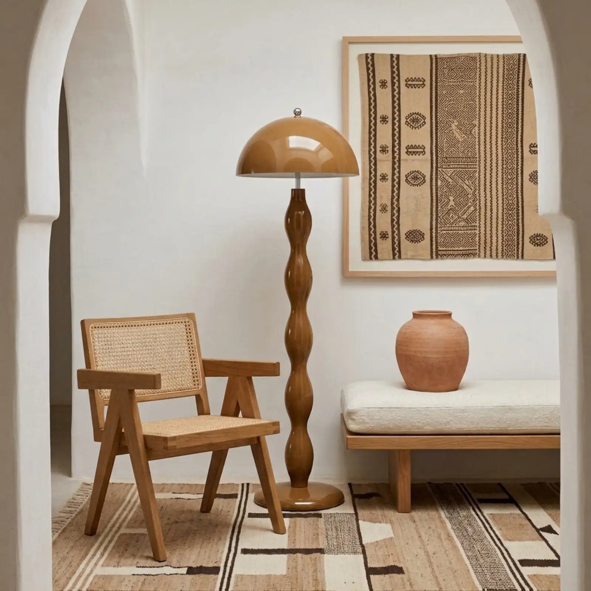 Lampadaire marron sous une arche blanche de style tunisien, près d'une chaise en cannage et d'une jarre en terre cuite