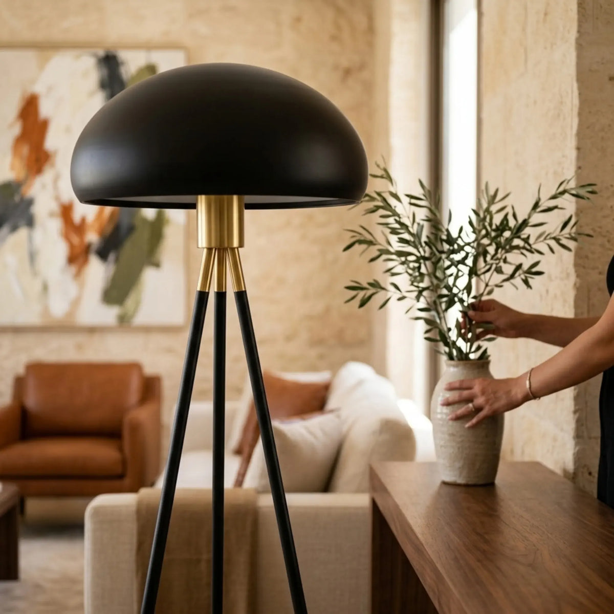 Détail du dôme noir mat et de la bague laiton du lampadaire, devant un fauteuil cognac et un tableau abstrait