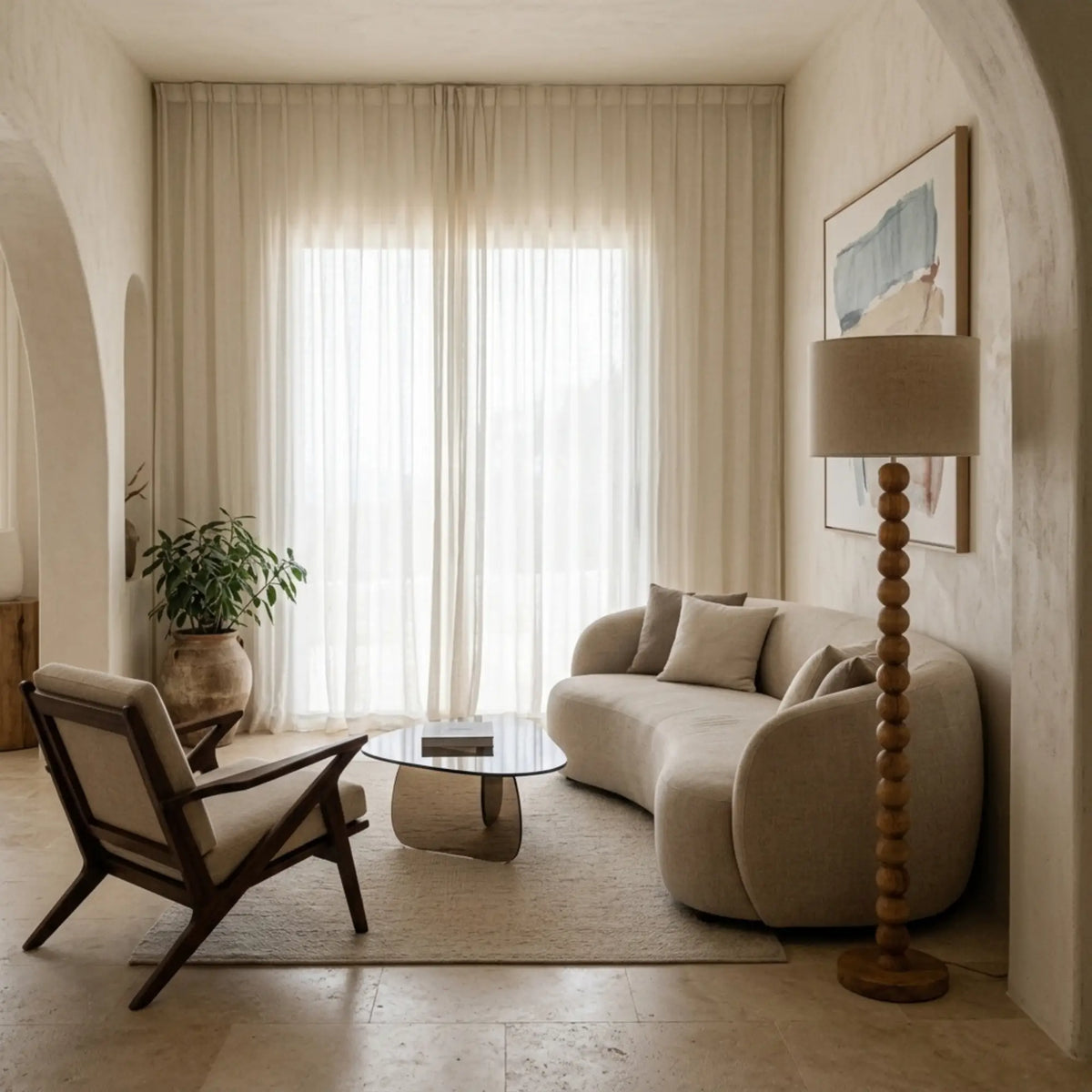 Lampadaire pied boule près d'un canapé arrondi crème et d'un fauteuil en bois, sous une arche aux murs clairs