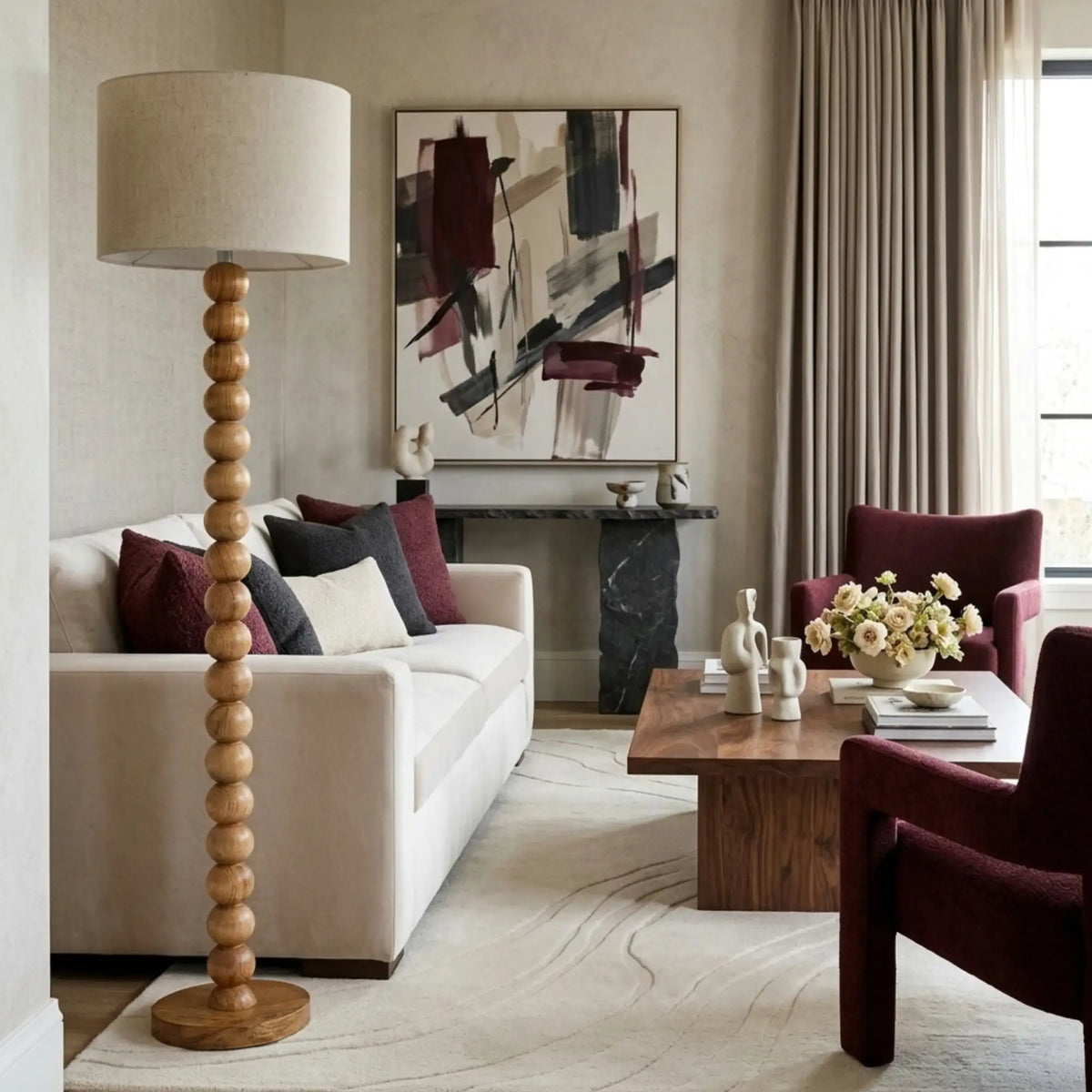 Lampadaire pied boule à côté d'un canapé blanc, fauteuils en velours bordeaux et table basse en bois, cheminée en pierre sombre au fond