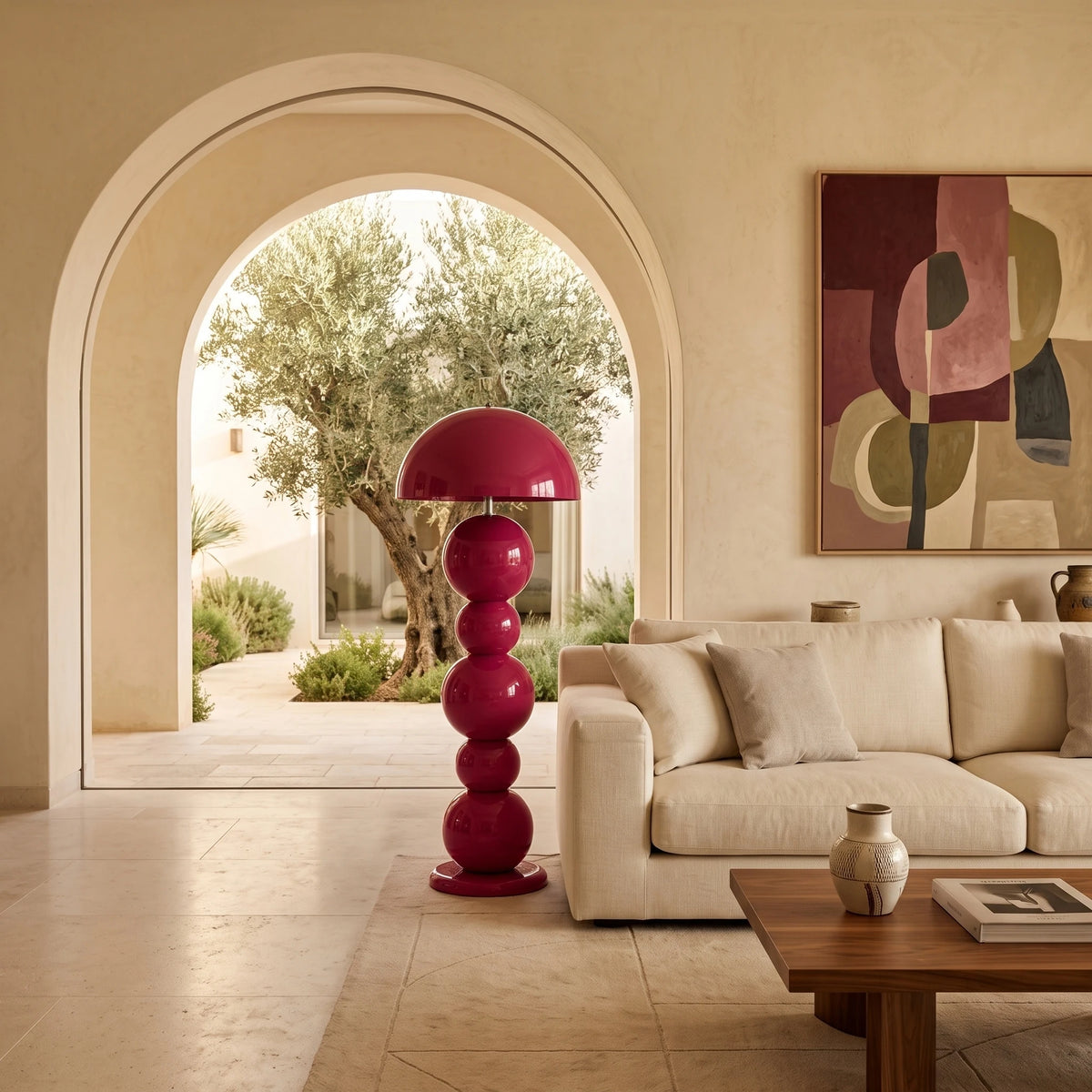Lampadaire rose fuchsia à boules près d'un canapé écru, devant une arche ouverte sur un patio avec olivier