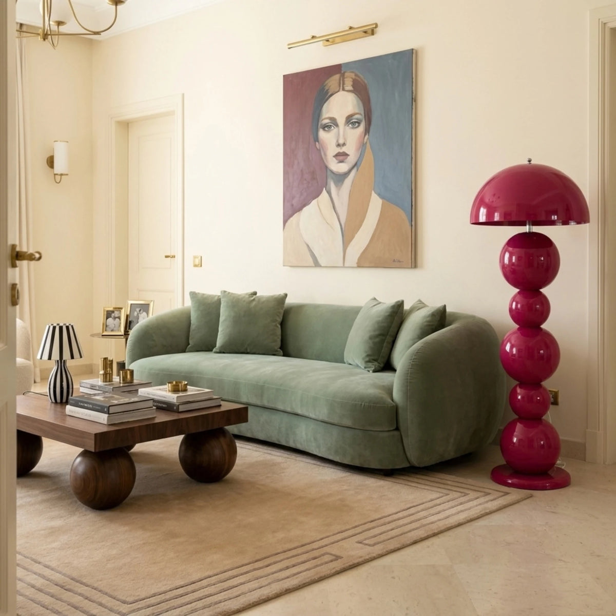 Lampadaire rose à boules à côté d'un canapé en velours vert sauge, sous un portrait peint