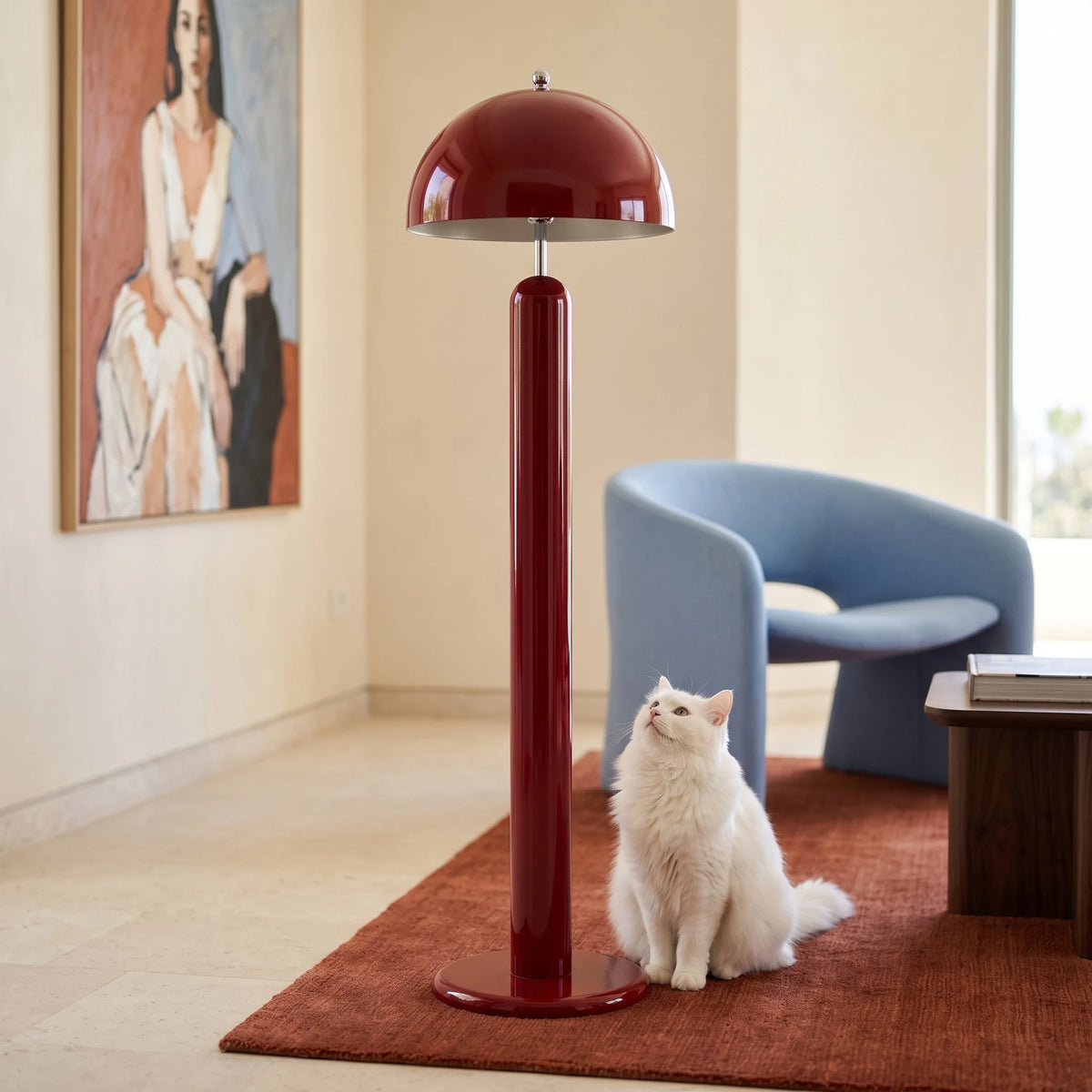 Lampadaire rouge carmin sur un tapis rouge, à côté d'un fauteuil bleu ciel et d'un chat blanc