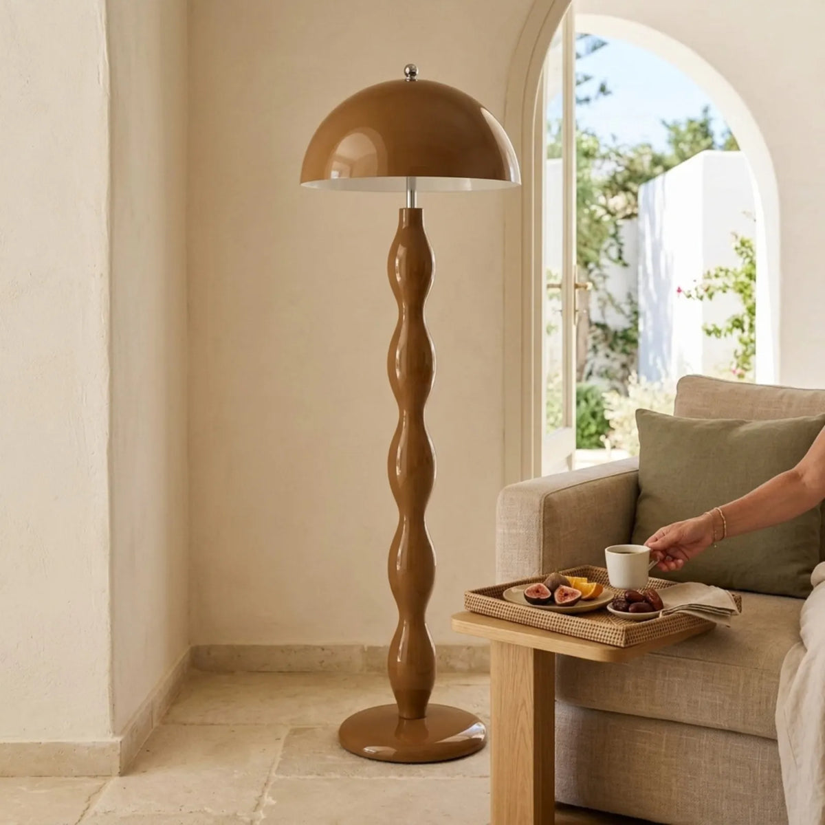 Lampadaire marron dans un salon blanc de style tunisien, à côté d'un canapé en lin et d'une porte en arc ouverte sur le jardin
