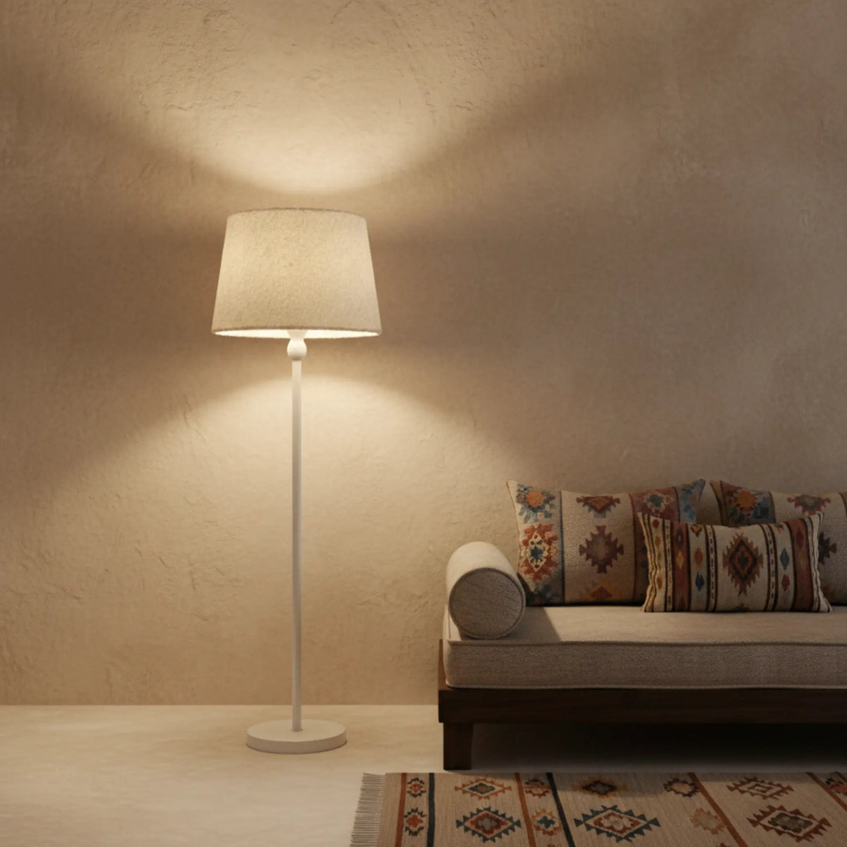 Lampadaire blanc allumé diffusant une lumière chaude au-dessus d'une banquette aux coussins kilim et d'un tapis tissé