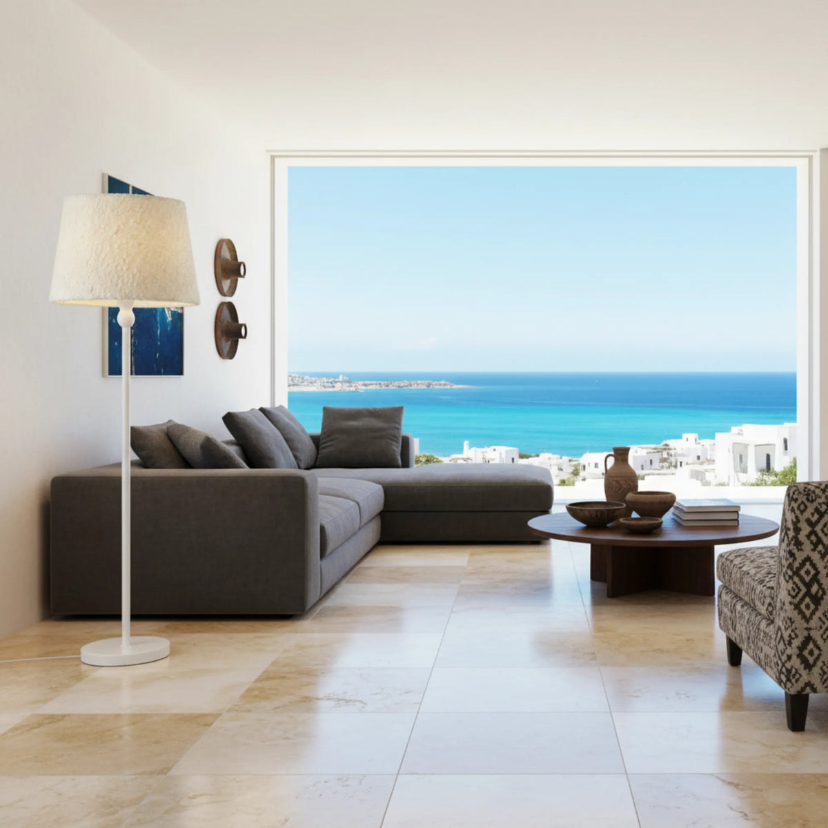 Lampadaire blanc dans un salon lumineux avec canapé d'angle gris et grande baie vitrée sur la mer