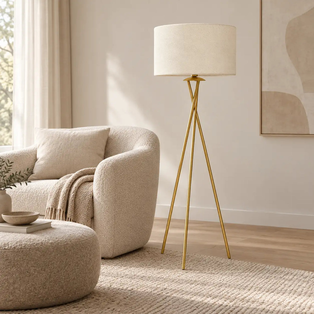 Lampadaire trépied doré derrière un fauteuil bouclé arrondi et son repose-pieds, sur un tapis crème