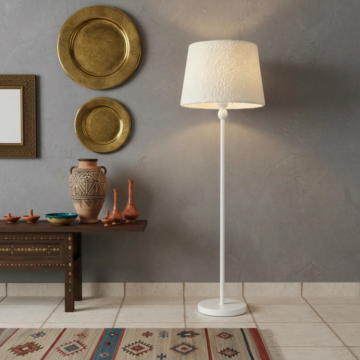 Lampe sur pied blanche allumée devant un mur gris décoré de plateaux dorés, à côté d'une console en bois et de poteries