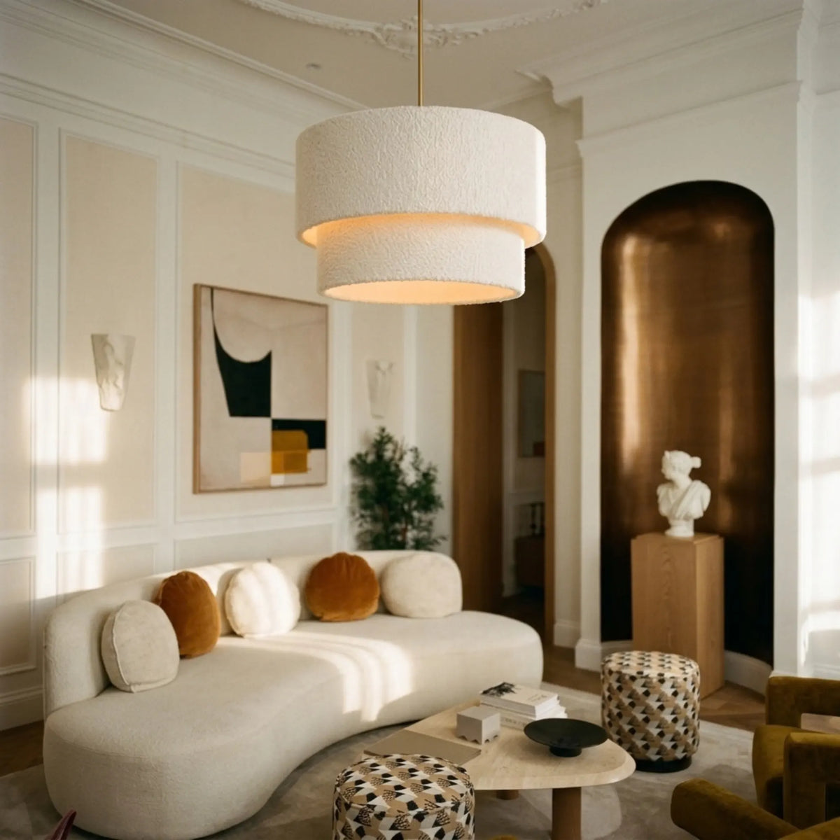 Lustre en tissu bouclette au-dessus d'un canapé arrondi écru, dans un salon à moulures et niche dorée