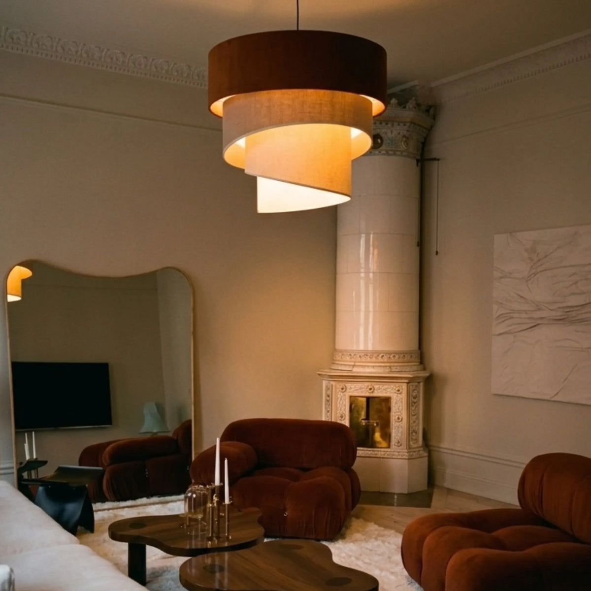 Lustre en velours terracotta dans un salon avec poêle en faïence et fauteuils en velours rouille
