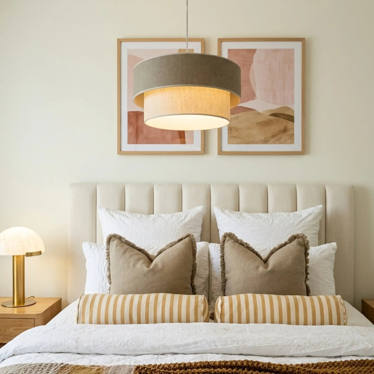 Suspension taupe et beige devant deux cadres aquarelle, au-dessus d'un lit à coussins rayés