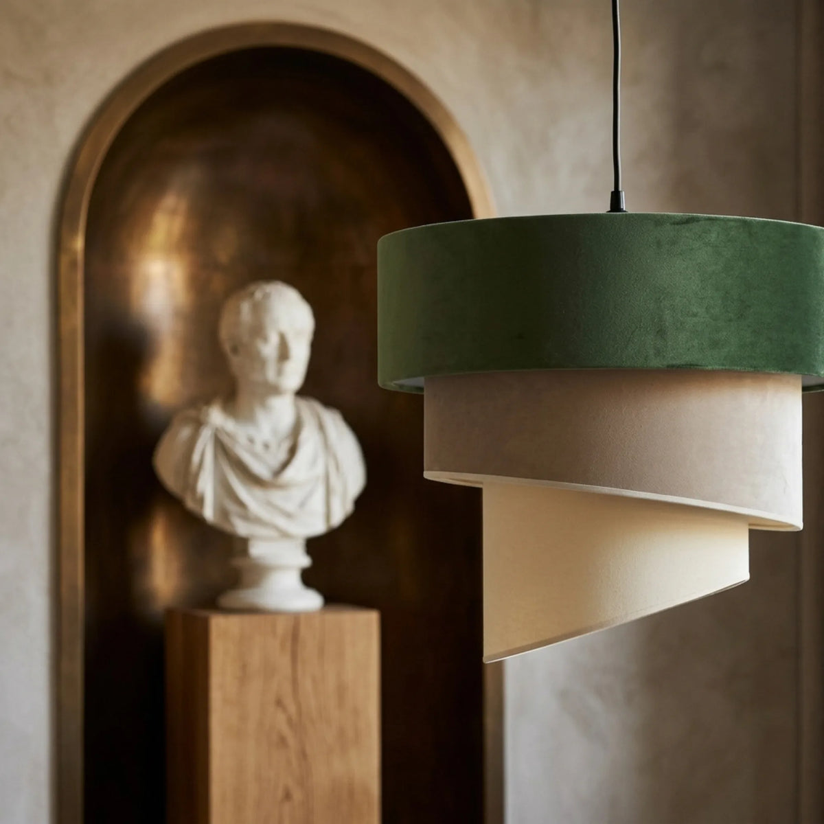 Gros plan sur le lustre en velours : tambour vert olive et volutes beige et crème, buste en arrière-plan