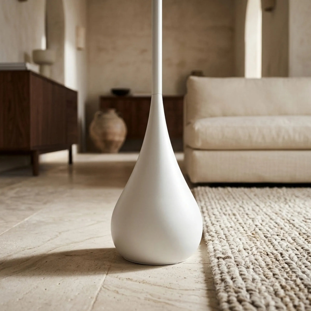 Gros plan sur la base en goutte d'eau blanc mat du lampadaire, posée sur un sol en pierre près d'un tapis