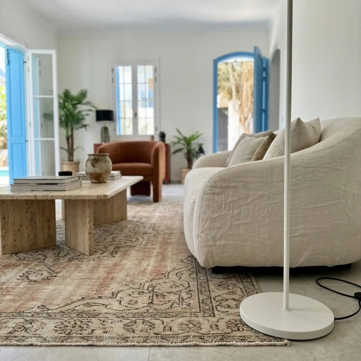 Détail de la tige fine et du socle rond blanc du lampadaire, sur un tapis ancien près d'un canapé blanc