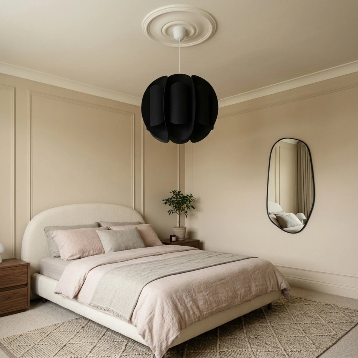 Suspension boule noire dans une chambre aux tons rose poudré et miroir ondulé