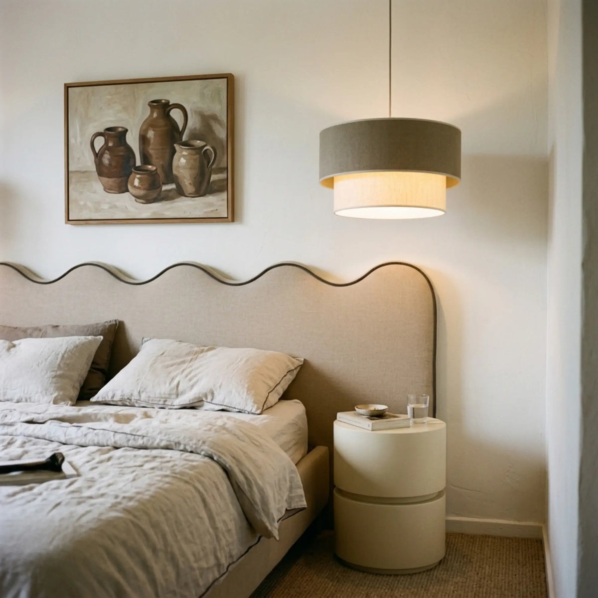 Suspension double tambour allumée près d'un lit à tête de lit ondulée en lin et chevet crème
