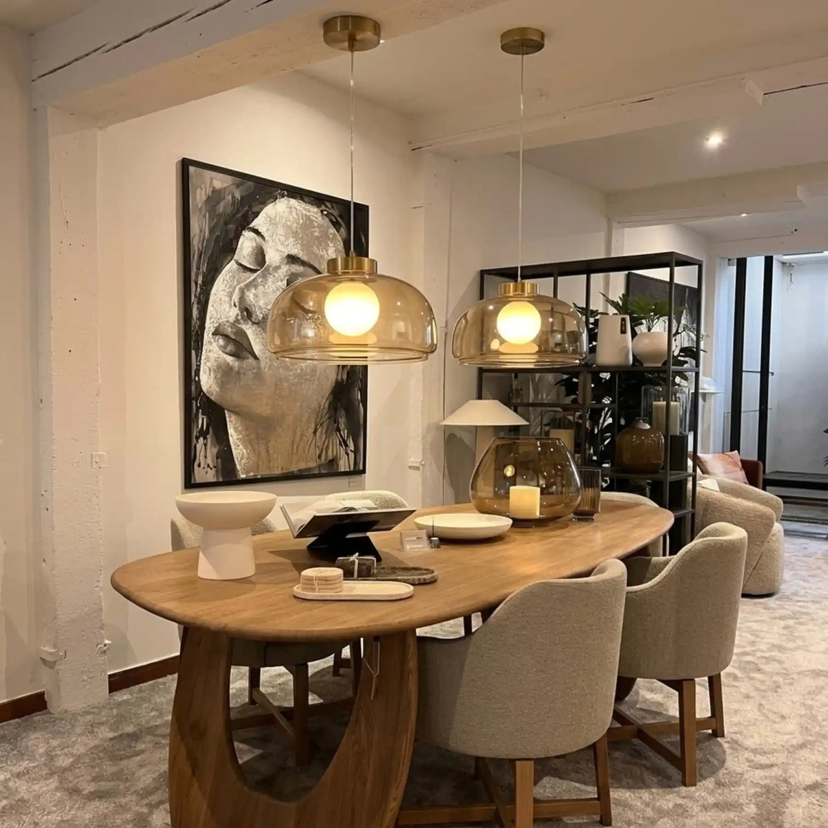 Duo de lustres en verre fumé doré au-dessus d'une table ovale en bois, fauteuils beiges et portrait au mur