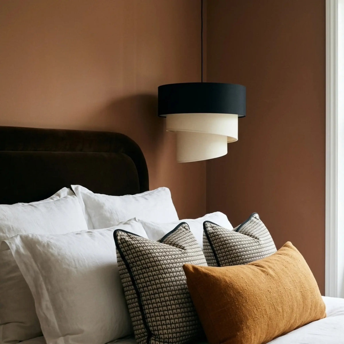 Suspension en spirale noir et écru dans une chambre au mur terracotta, coussins graphiques sur le lit