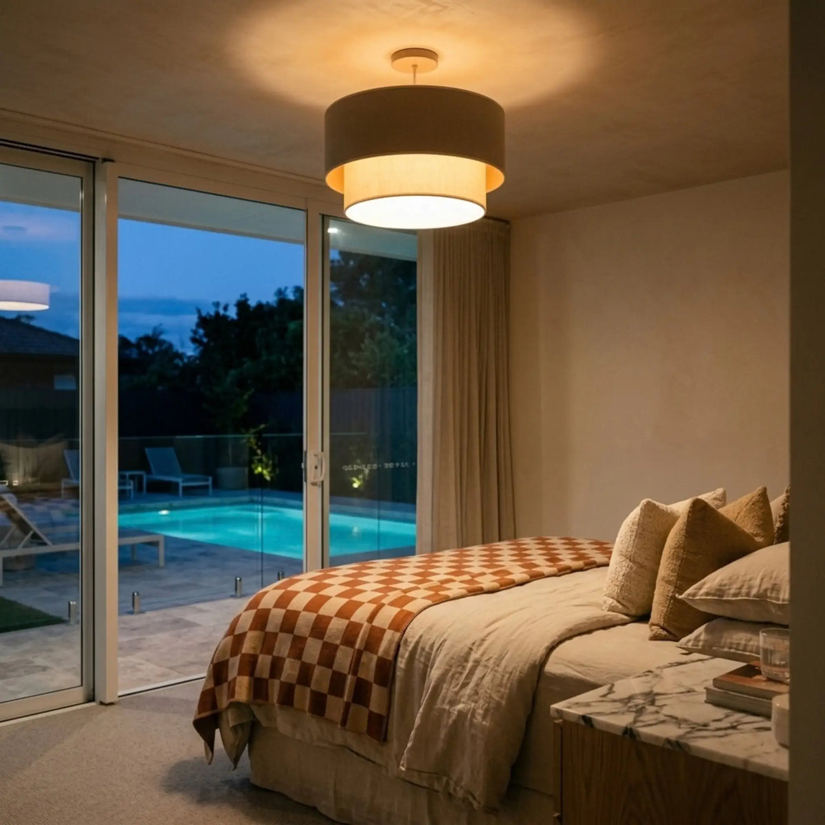 Suspension taupe allumée le soir dans une chambre ouverte sur une terrasse avec piscine