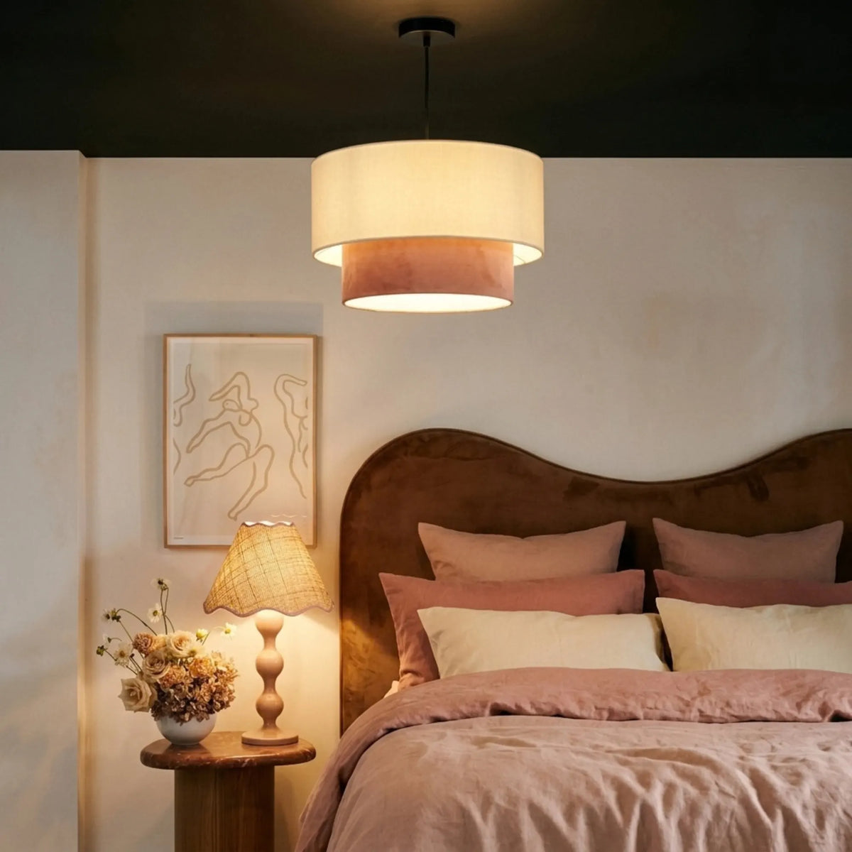 Suspension beige et vieux rose allumée sous un plafond sombre, au-dessus d'un lit aux tons poudrés